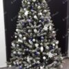 Umělý vánoční stromek Smrk Křišťálový 180cm je zdoben bílými, fialovými a modrými dekoracemi.