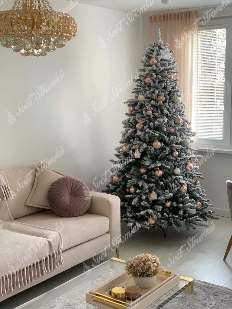 Zasněžený vánoční stromek ozdobený zlatými a pudrovými vánočními ozdobami.