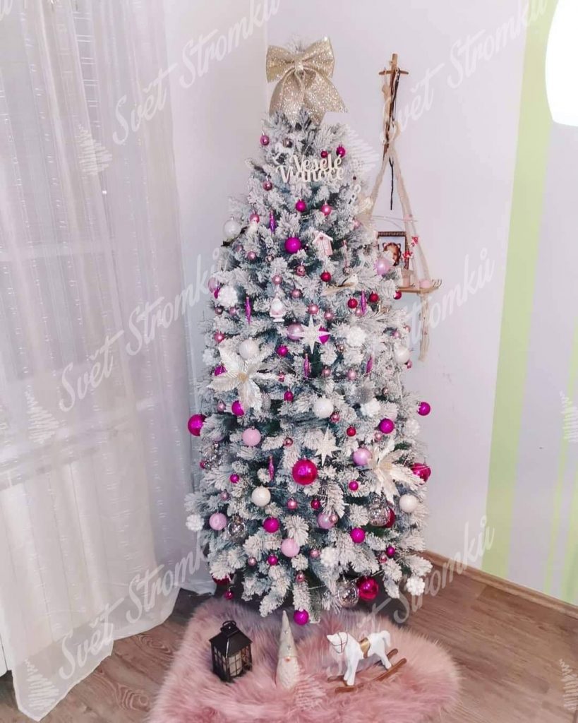 Bílý vánoční stromek ozdobený růžovými a bílými koulemi spolu s bílými hvězdičkami.