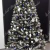 Vánoční stromek s jemně zasněženými konečky větviček ozdobený bílými a modrými vánočními ozdobami.