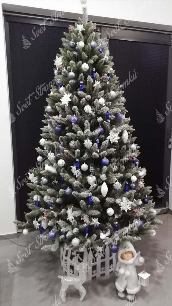 Vánoční stromek s jemně zasněženými konečky větviček ozdobený bílými a modrými vánočními ozdobami.