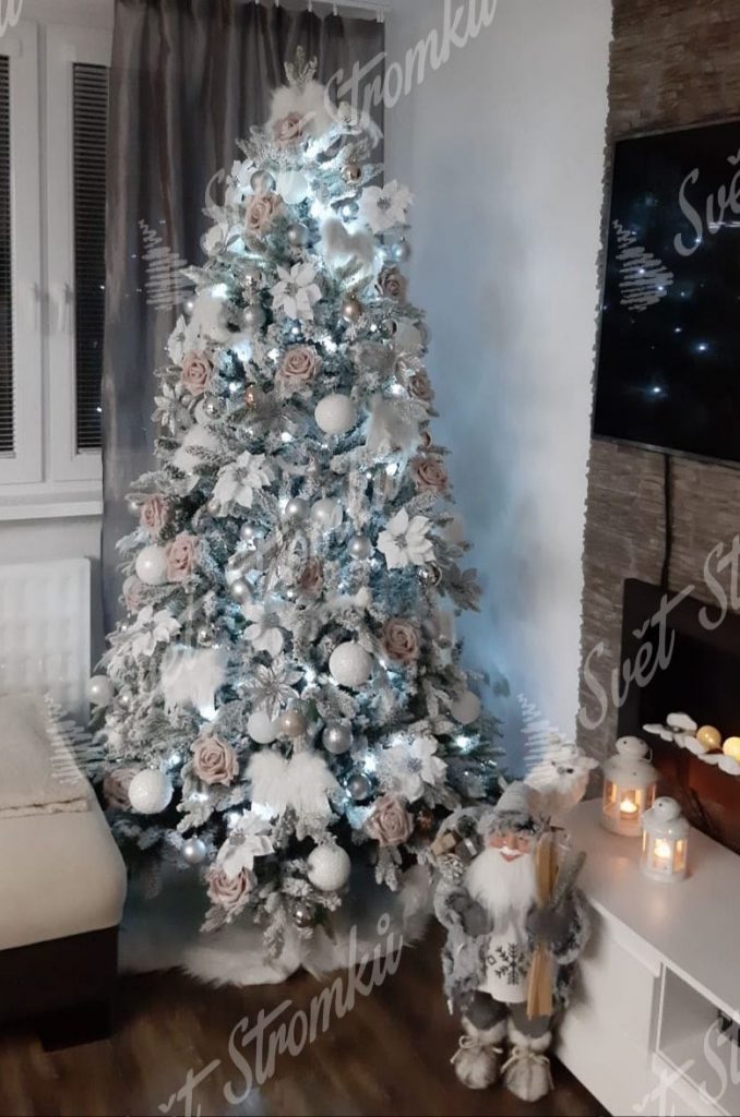 Bíly zasněžený vánoční stromek ozdobený bílými koulemi a květy spolu s andělskými křídly.