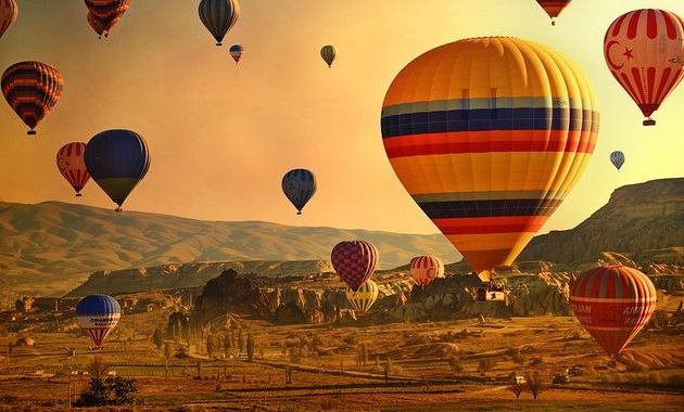 Kolem 17 horkovzdušných balónů v různých barevných provedeních nad krásnou přírodou.