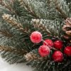 Detail vánočního věnečku pokrytého bílými chomáčky, borovými šiškami a červenými lesními plody.