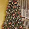 Zelený umělý vánoční stromeček, ozdobený červenými a přírodními ozdobami a teplým bílým osvětlením, v obýváku