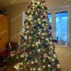 Zelený umělý vánoční stromeček s tmavozelenými větvičkami, ozdobený barevnými ozdobami a teplým bílým osvětlením, v obýváku