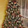 Zelený umělý vánoční stromeček s tmavozelenými větvičkami, ozdobený červenými a přírodními ozdobami a teplým bílým osvětlením, v obýváku