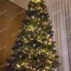Zelený umělý vánoční stromeček s tmavozelenými větvičkami, ozdobený stříbrno-fialovými ozdobami a teplým bílým osvětlením, v obýváku
