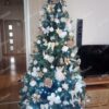 Zelený umělý vánoční stromek s tmavozelenými větvičkami, ozdobený bílo-zlatými ozdobami a bílým osvětlením, v obýváku