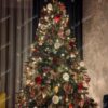 Umělý vánoční stromeček se zelenými větvičkami, ozdobený červenými a přírodními ozdobami a teplým bílým osvětlením, v rohu obývacího pokoje