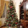 Zelený umělý vánoční stromeček, hustě ozdobený červeno-zlatými ozdobami a teplým bílým osvětlením, v rohu obývacího pokoje