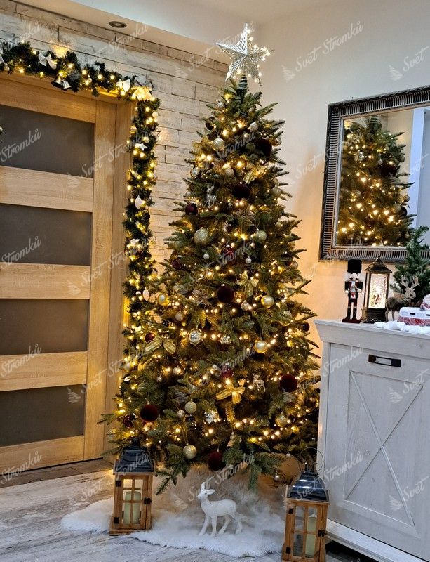 Umělý vánoční stromeček s bledě zelenými hustými větvičkami, ozdobený zlatými ozdobami a teplým bílým osvětlením, v rohu obývacího pokoje