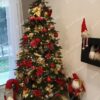 Zelený umělý vánoční stromeček, ozdobený červeno-zlatými ozdobami a teplým bílým osvětlením, v rohu obývacího pokoje