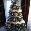 Široký a mohutný umělý vánoční stromeček se zelenými větvičkami, ozdobený bílými ozdobami, v rohu obývacího pokoje