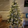 Umělý vánoční stromeček s hustými zelenými větvičkami, ozdobený bílými ozdobami, s teplým bílým osvětlením, v obýváku