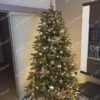 Zelený umělý vánoční stromek, ozdobený zlato-měděnými ozdobami, s teplým bílým osvětlením, v obýváku