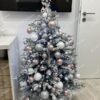 Nízký umělý zasněžený vánoční stromeček, ozdobený bílo-růžovými a stříbrnými ozdobami, v obýváku