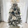 Bílý umělý vánoční stromeček, s hustě zasněženými větvičkami, ozdobený bílými ozdobami, u okna v obýváku