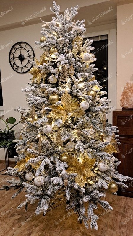 Umělý vánoční stromeček s hustě zasněženými větvičkami, ozdobený bílo-zlatými ozdobami, s teplým bílým osvětlením, v obýváku