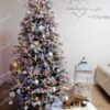 Zasněžený umělý vánoční stromek, hustě ozdobený bílo-růžovými ozdobami, s bílým koberečkem pod stromeček, v obýváku