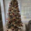 Zasněžený umělý vánoční stromeček, elegantně ozdobený červeno-bílými ozdobami, s teplým bílým osvětlením, v rohu obývacího pokoje