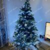 Zelený umělý vánoční stromek, ozdobený bílo-zaltými ozdobami a bílým osvětlením, v obýváku
