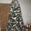 Vysoký tmavě zelený umělý vánoční stromeček, hustě ozdobený barvenými ozdobami, v obýváku