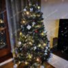 Umělý vánoční stromeček se stříbrnými konci větviček, ozdobený červeno-bílými ozdobami a teplým bílým osvětlením, v rohu obývacího pokoje