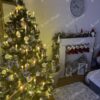 Umělý vánoční stromeček se stříbrnými konci větviček a dekorací krystalů ledu, ozdobený zlato-bílými ozdobami, s teplým osvětlením, v obýváku u krbu