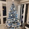 Bílý umělý vánoční stromek se zasněženými větvičkami, ozdobený bílými ozdobami, se studeným bílým osvětlením, v obýváku