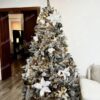 Zasněžený umělý vánoční stromeček s bílo-zlatými ozdobami a vánočními růžemi, s teplým bílým osvětlením, v obýváku