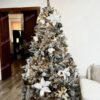 Umělý vánoční stromek se zasněženými větvičkami, ozdobený zlato-bílými ozdobami a vánočními růžemi, s teplým bílým osvětlením, v obýváku