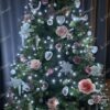 Zelený umělý vánoční stromeček, ozdobený bílo-růžovými ozdobami, s bílým osvětlením, v obýváku
