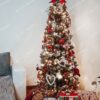 Zelený úzký umělý vánoční stromeček, ozdobený červeno-bílými ozdobami, s teplým bílým osvětlením, v obýváku