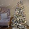 Nízký umělý vánoční stromeček se zasněženými větvičkami, ozdobený bílo-růžovými větvičkami, s teplým bílým osvětlením, v obýváku