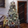 Zasněžený umělý vánoční stromeček, ozdobený bílo-červenými ozdobami, s teplým bílým osvětlením, v obýváku