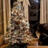Bílý vánoční stromek s hustě zasněženými větvičkami, ozdobený velkými vánočními ozdobami, s bílým osvětlením, v obýváku