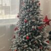 Bílý umělý vánoční stromeček s hustě zasněženými větvičkami, ozdobený červenými ozdobami, se zabudovaným LED osvětlením, v obýváku