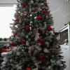 Bílý umělý vánoční stromeček s hustě zasněženými větvičkami, ozdobený červeno-bílými ozdobami, v obýváku