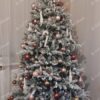 Hustě zasněžený umělý vánoční stromeček, ozdobený růžovo-zlato-měděnými ozdobami, v obýváku