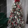 Umělý vánoční stromeček s hustě zasněženými větvičkami, ozdobený červeno-bílými ozdobami, v obýváku