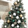 Nízký umělý vánoční stromeček se stříbrnými větvičkami, ozdobený zlatými, bílými a tmavě zelenými ozdobami, v obýváku