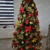 Umělý vánoční stromeček s tmavozelenými větvičkami, ozdobený velkými červeno-zlatými ozdobami a mašlemi, v obýváku