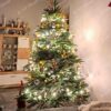 Umělý vánoční stromeček se světle zelenými větvičkami, ozdobený dřevěnými ozdobami, teplým bílým osvětlením, v obýváku
